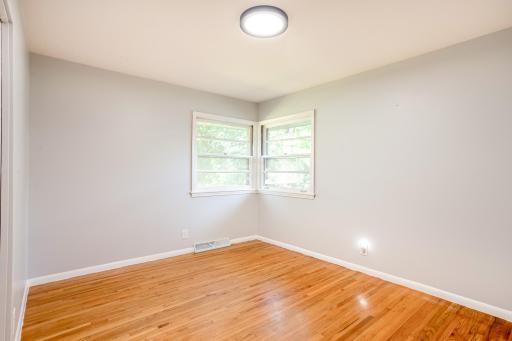 Cozy second bedroom featuring natural light from wraparound corner windows and pristine wood floors.