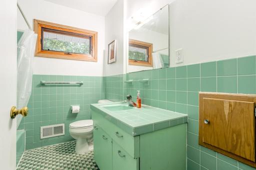 Retro-style bathroom with original green tilework, built-in vanity, and upper window for ventilation.