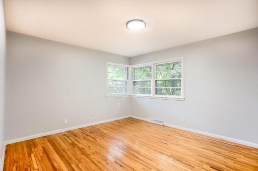 Spacious primary bedroom with warm hardwood flooring and double corner windows offering treetop views.
