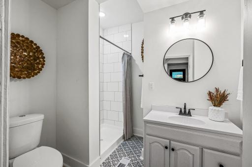 The main floor 3/4 bathroom features a stunning tiled shower, stylish patterned flooring, and modern lighting paired with sleek black hardware you're sure to love.