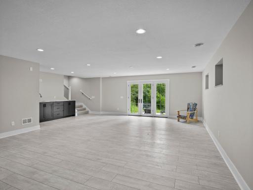 Spacious lower level family room / entertainment space with wet bar and walk-out to patio, woods, and path leading down to the river