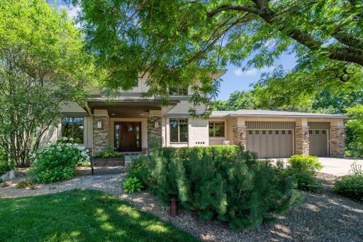 Crisp daytime view of the home’s inviting façade with a stone and stucco finish, three-car garage, manicured landscaping, and charming flower beds.