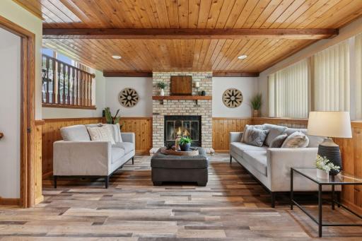 Warm and welcoming family room featuring a cozy brick fireplace, wood-paneled ceiling and walls, and large windows that fill the space with natural light â perfect for relaxing or entertaining.