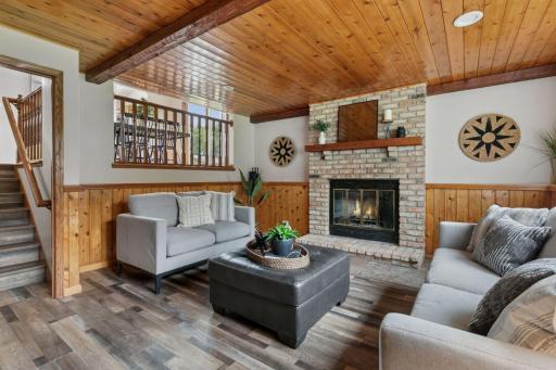 Warm and welcoming family room featuring a cozy brick fireplace, wood-paneled ceiling and walls, and large windows that fill the space with natural light â perfect for relaxing or entertaining.