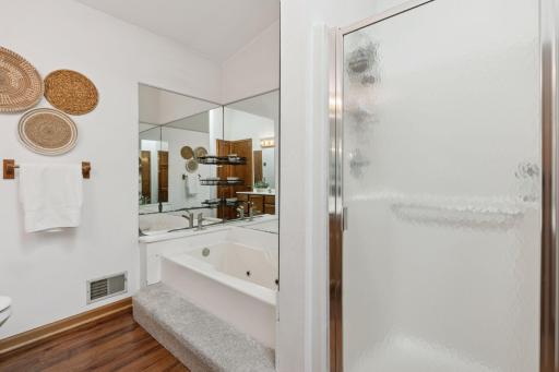 Primary bathroom with vaulted ceiling and skylight, showcasing natural wood vanity, wood-style luxury vinyl plank flooring, and a relaxing jetted tub for a spa-like experience.