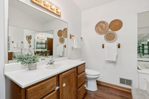 Primary bathroom with vaulted ceiling and skylight, showcasing natural wood vanity, wood-style luxury vinyl plank flooring, and a relaxing jetted tub for a spa-like experience.