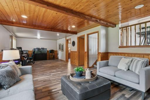 Warm and welcoming family room featuring a cozy brick fireplace, wood-paneled ceiling and walls, and large windows that fill the space with natural light â perfect for relaxing or entertaining.