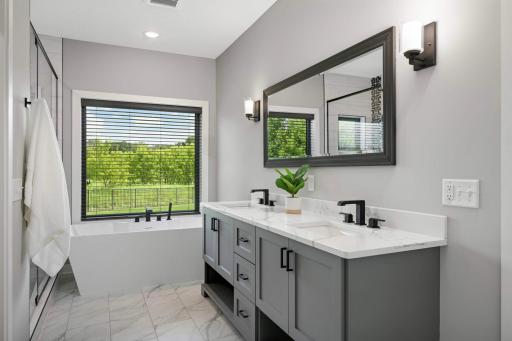 Beautiful full bathroom features: a double sink vanity, soaking tub with a picture window looking out the backyard, a water closet, large walk-in closet, and a spacious tiled walk-in shower with glass door.