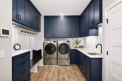 Main level laundry and mudroom complete with pedestals under the washer and dryer, undercabinet lighting, utility sink, bench and hooks for coats, tons of cabinets for storage, and even hidden drying racks in two of the cabinets.