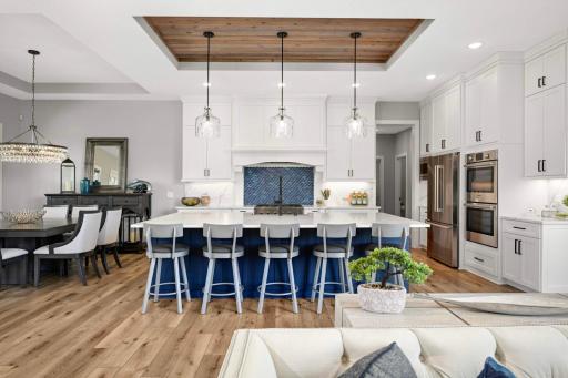 Chefâs kitchen features a large island with quartz countertops, Bosch stainless appliances (gas cooktop, refrigerator, dishwasher, double oven), and a beautiful range hood with tiled backsplash underneath.