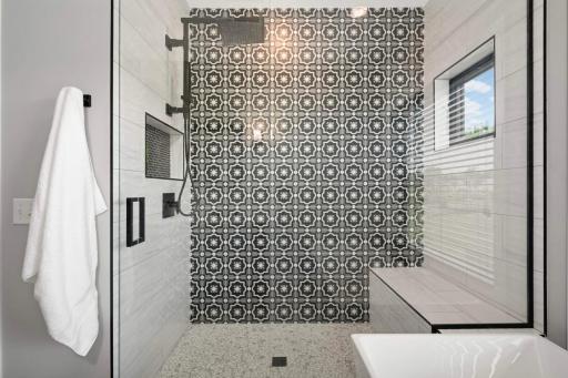 Stunning fully tiled walk-in shower with bench, a glass door, and window looking outside.
