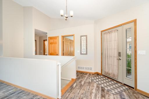 Welcome your guests in this 9.10x8 foyer with updated: flooring, paint, door hardware & chandelier. From right to left, this photo also shows the guest bedroom, the coat closet, and a hallway leading to the 1/2 bathroom & the primary bedroom suite.