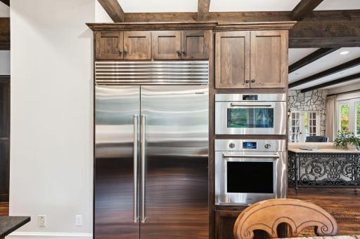 Top-of-the-line Sub-Zero refrigerator and Wolf double ovens complement the custom cabinetry and exposed beams, offering both function and elegance in this chef-inspired luxury kitchen.
