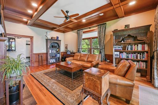 This elegant den at the front of the home features a coffered ceiling, hardwood floors, and a wood-burning fireplaceâideal as a study with views of both the lake and the gated drive.