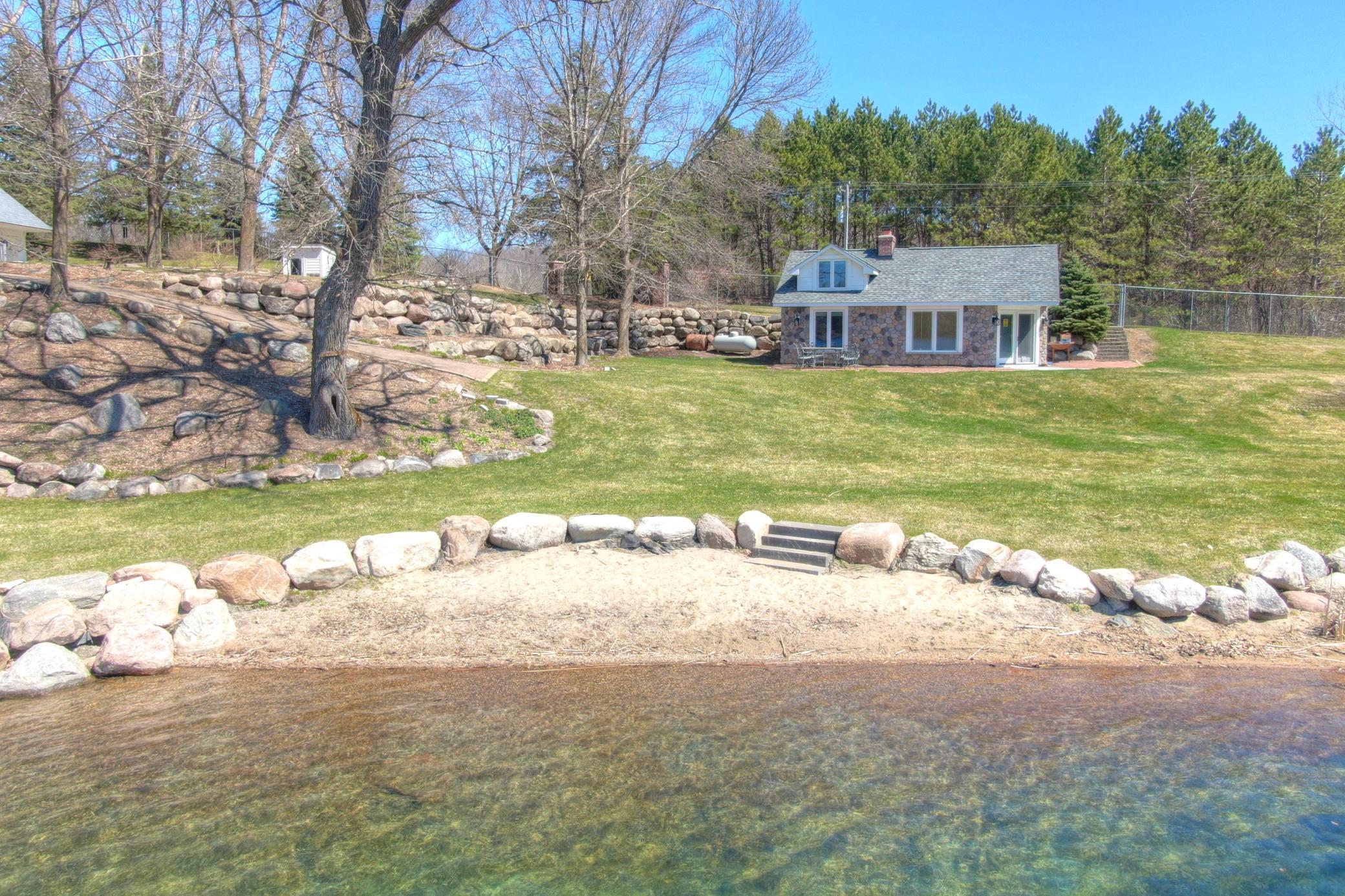 The charming lakeside guest cottage features updated stonework and siding 2020-2021 with the sand beach landscaping added at that time as well. New roof in 2025 along with an interior refresh of flooring, tongue and groove plus paint.