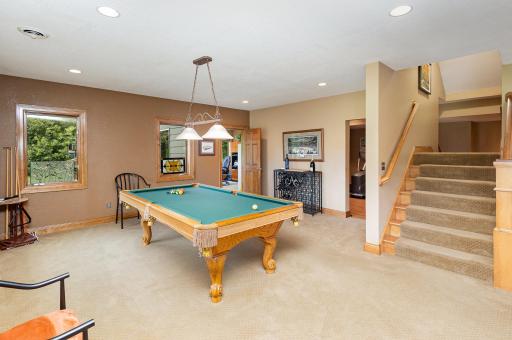 As you enter the walkout lower level, a split staircase creates a dramatic first impression, opening into a spacious recreational area. From this inviting vantage point, the view extends toward the fifth bedroom.