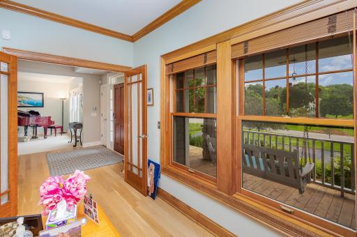 From the office just off the front porch, a welcoming view unfolds through the airy foyer and into the inviting living room beyond, where classic architectural lines and natural flow create a sense of openness.