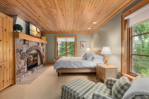 A custom stone fireplace identical to the fireplace in the living room centers the primary suite and the wood slat ceilings offer comfort and gorgeous design.