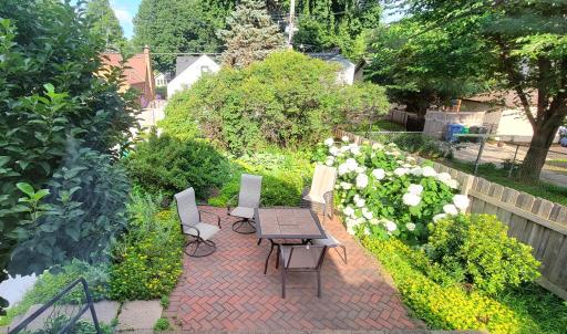The herringbone pattern brick patio is surrounded by shrubs and perennials for beautiful and private outdoor entertaining.
