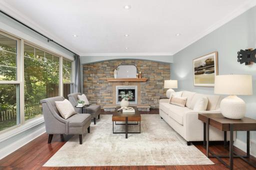 This main level family room features a welcoming & airy design, highlighted by a full wall of large windows that bring in natural light & showcase a view of the lush, private back yard. The focal point is a stone fireplace wall with wood mantel.