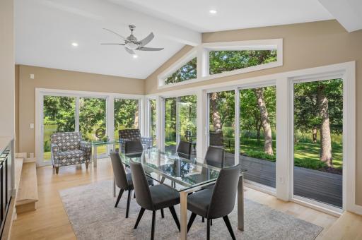 Window lined formal dining room with patio doors that open to the lakeside deck.