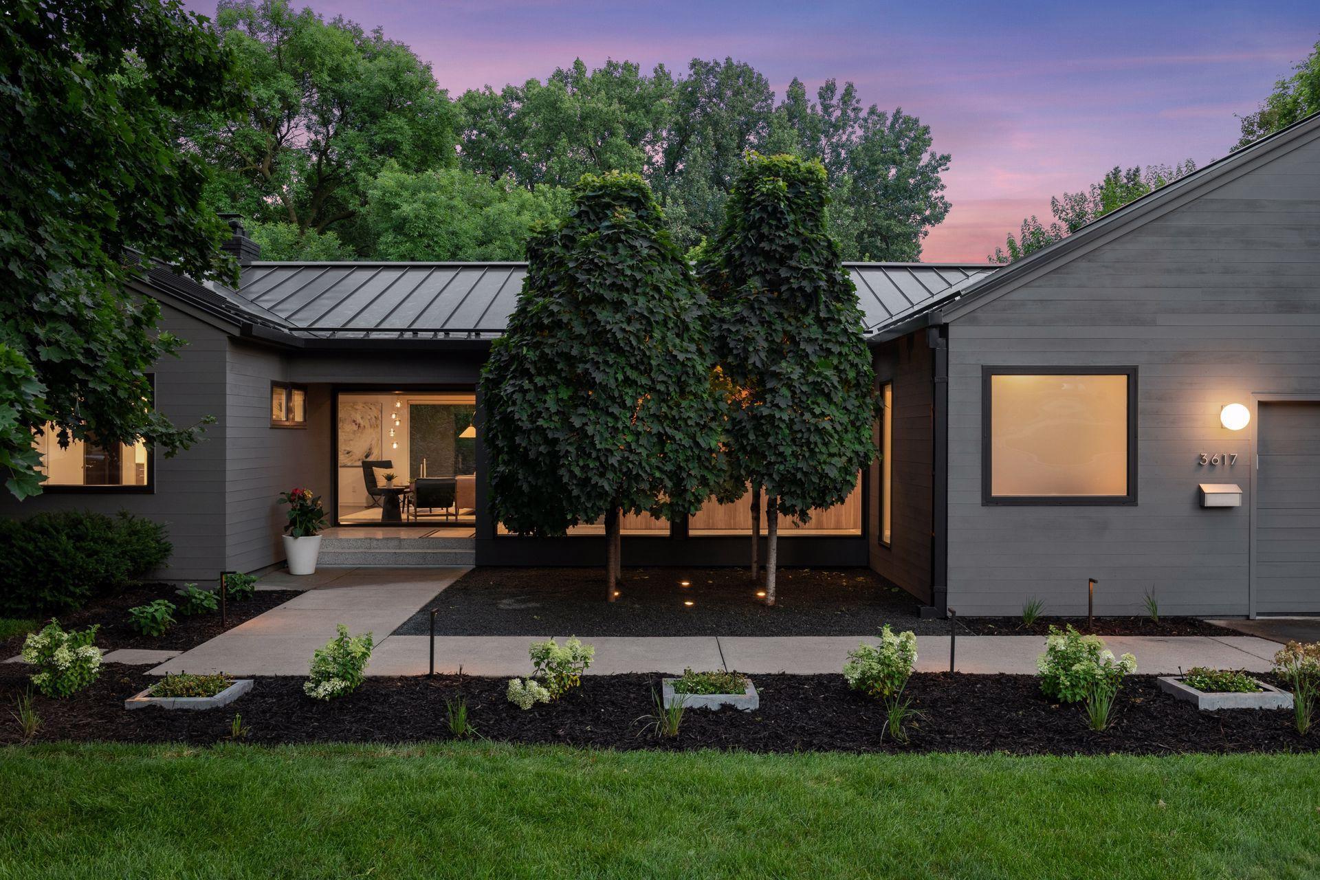 Dusk setting over this mid-century modern rambler with a standing seam metal roof & stunning landscaping