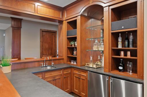 Beautiful wood cabinetry and stylish countertops of this custom bar add a touch of elegance to the lower level entertainment space.