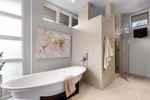 Spa-like ensuite bathroom featuring dual granite vanities, heated floors, pedestal tub, and river rock walk-in shower.
