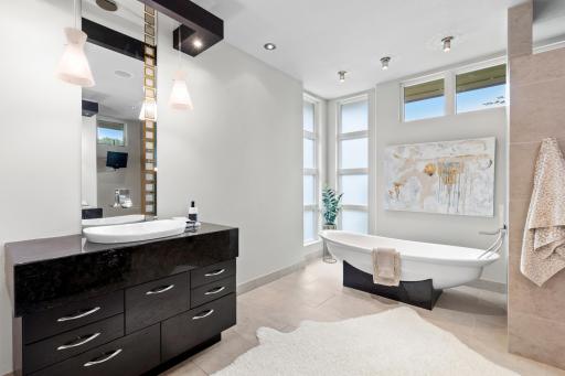 Spa-like ensuite bathroom featuring dual granite vanities, heated floors, pedestal tub, and river rock walk-in shower.