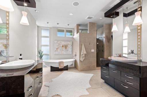 Spa-like ensuite bathroom featuring dual granite vanities, heated floors, pedestal tub, and river rock walk-in shower.