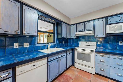 Just beyond, the kitchen combines style and practicality with its eye-catching cabinetry, tile countertops and backsplash, ample storage, and a window that fills the space with light.