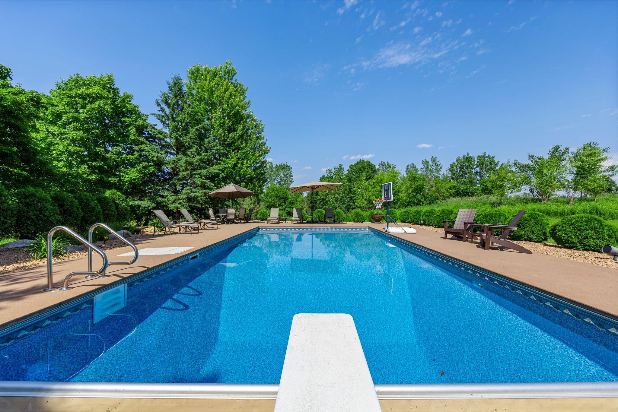 Resort-style pool with diving board, basketball hoop, and expansive patio—perfect for relaxing or entertaining in total privacy. Surrounded by lush greenery and open views.