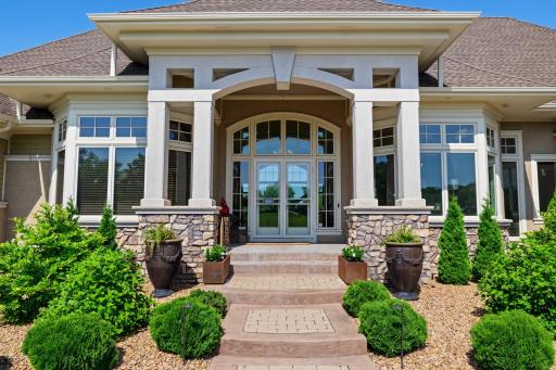 Grand front entry with arched transom windows, stone accents, and custom pillars creates a stunning first impression. Professionally landscaped with paver steps and curated greenery for a warm and welcoming arrival.