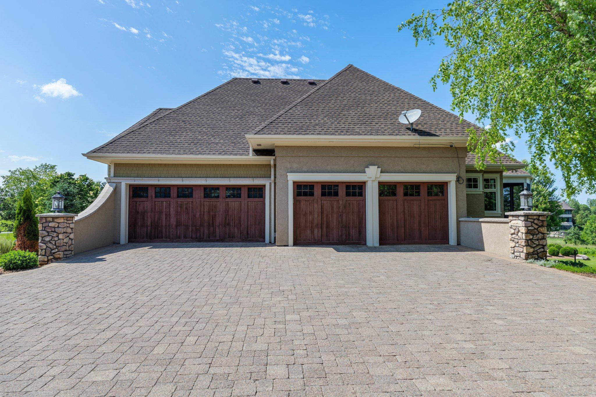 Paver driveway leads to an oversized 4-car garage with custom wood doors, stone accents, and ample space for vehicles, storage, or hobby use. Exceptional curb appeal with thoughtful design details and side-yard access.