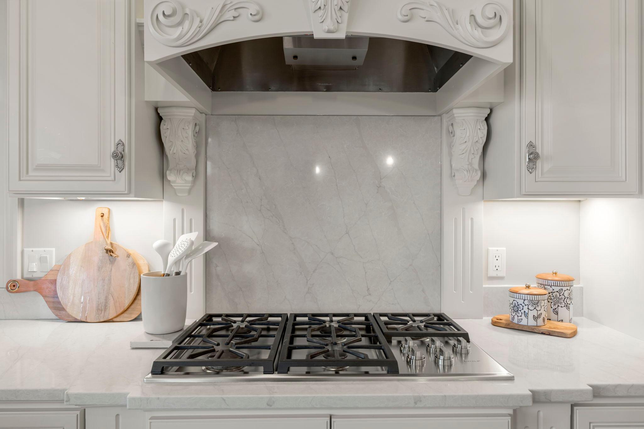 Cooktop with custom vent hood, marble backsplash, and built-in cabinetry. Functional layout with quality finishes and ample prep space.