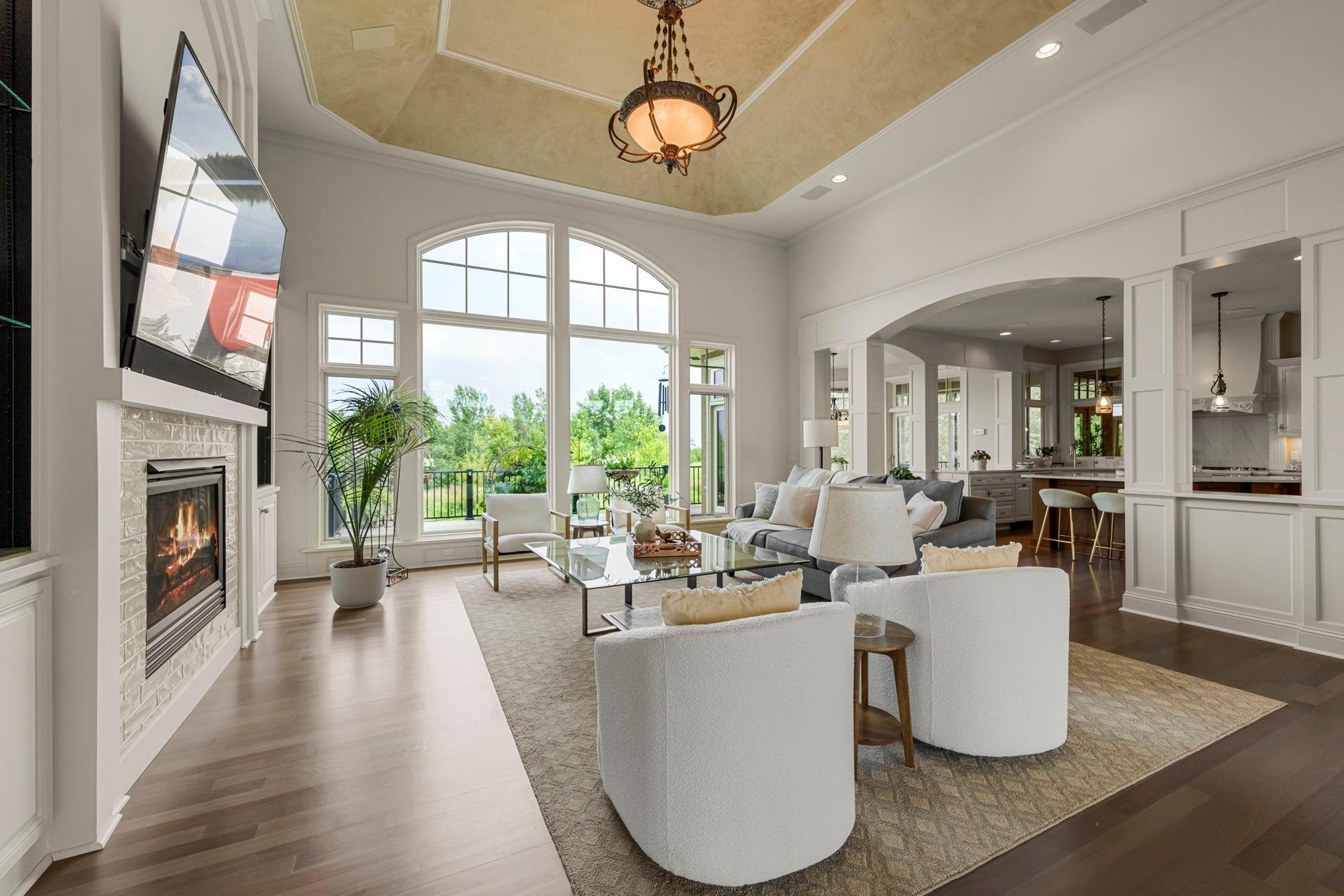 Light-filled great room with vaulted ceiling, gas fireplace, and expansive windows showcasing stunning meadow views. Seamless flow to the kitchen and dining areas makes this an ideal space for everyday living and entertaining.