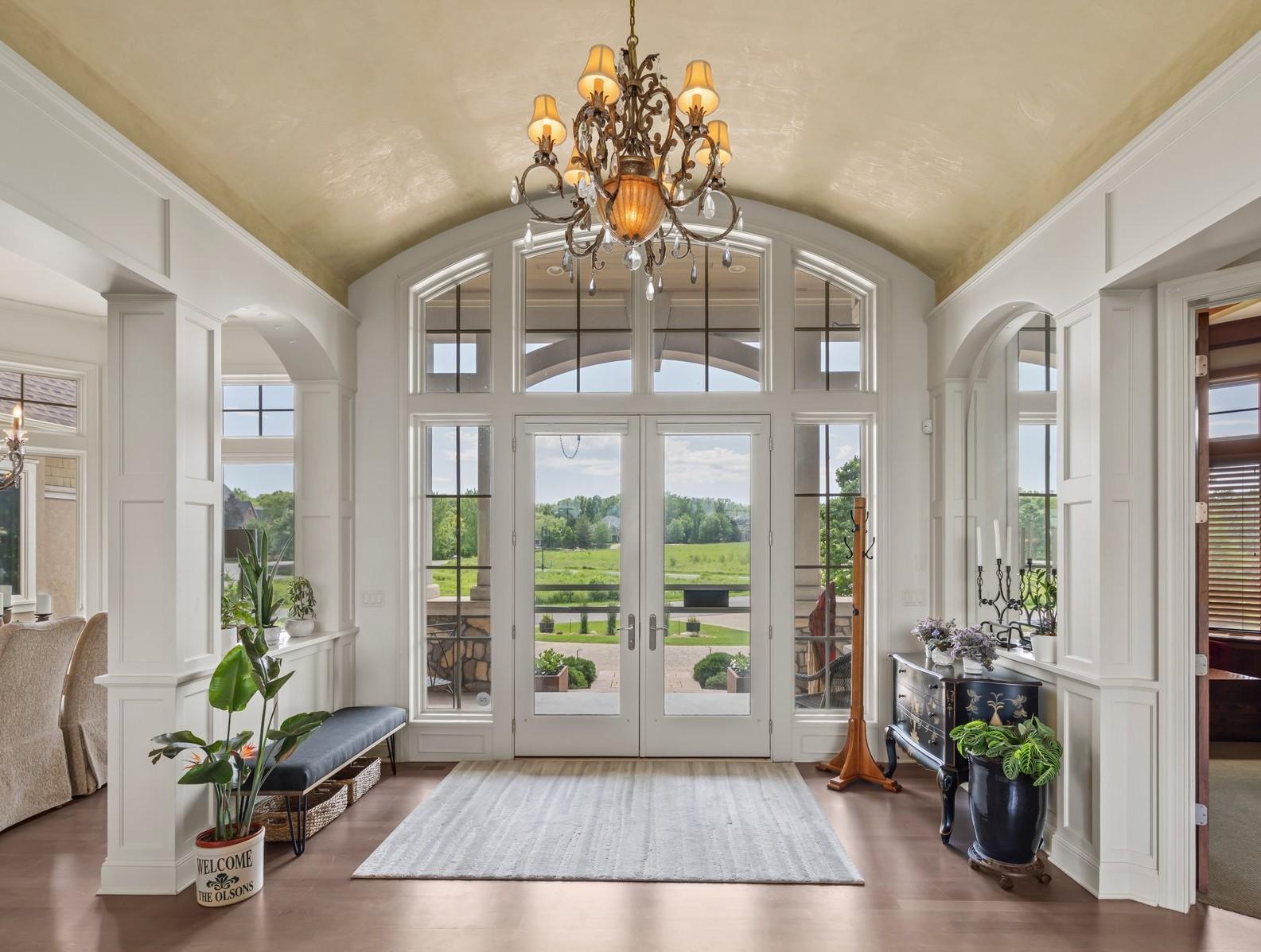Impressive front foyer with soaring vaulted ceiling and custom millwork. Floor-to-ceiling windows and arched transom above the front door flood the space with natural light and showcase views of the circular drive and manicured landscapaping.