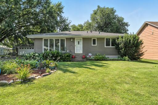Charming front exterior featuring a long driveway leading to a spacious two-car detached garage. Mature trees provide shade and curb appeal, while lush landscaping enhances the welcoming feel of this home.