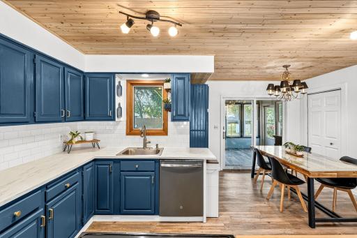 Bright kitchen with bold navy cabinetry, brass hardware, and white subway tile backsplash. A large window, complemented by a beautiful wood-paneled ceiling and updated lighting fixtures.