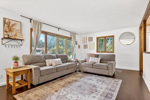 Bright and inviting living room featuring large picture windows that fill the space with natural light. Freshly painted walls, warm wood trim, and rich hardwood floors create a cozy yet stylish atmosphere.
