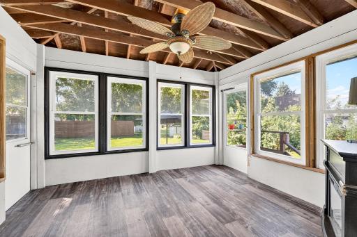 Bright and inviting sunroom with walls of windows offering stunning backyard views. The space features updated flooring and an overhead ceiling fan, making it an ideal spot for morning coffee or relaxing.