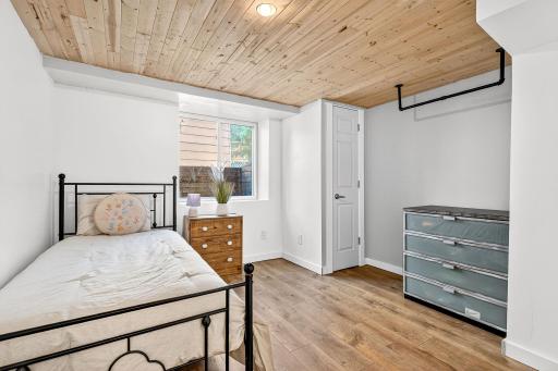 Comfortable lower-level bedroom #4 with large daylight window, natural wood ceiling detail and LVP floors. A cozy retreat.