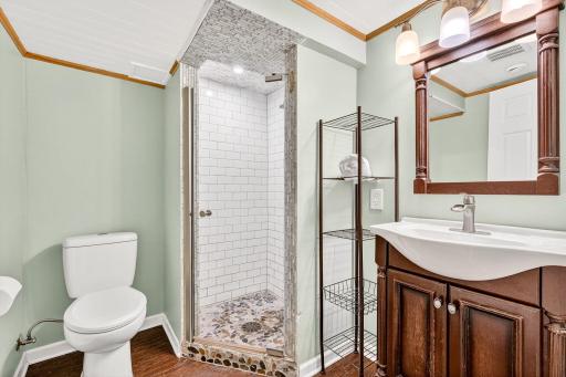 Updated lower-level ¾ bathroom showcasing a stylish walk-in shower with tile surround, pebble stone shower floor, and glass door. Modern vanity with elegant mirror completes the space.