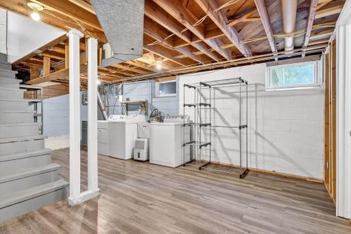 Bright and functional laundry area located in the basement, featuring a washer, dryer, utility sink, and plenty of open space for storage or future customization. Durable flooring adds practicality to this versatile space.