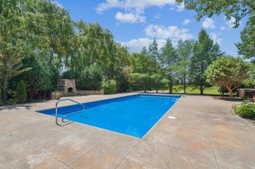 Private backyard oasis featuring an in-ground pool, expansive stamped concrete patio, and mature tree-lined backdrop—perfect for entertaining.