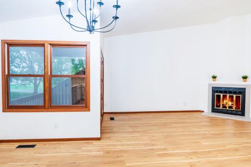 Bright and inviting living room showcasing gleaming new flooring, a cozy fireplace, vaulted ceilings and seamless access to a private balcony with lush, green views.
