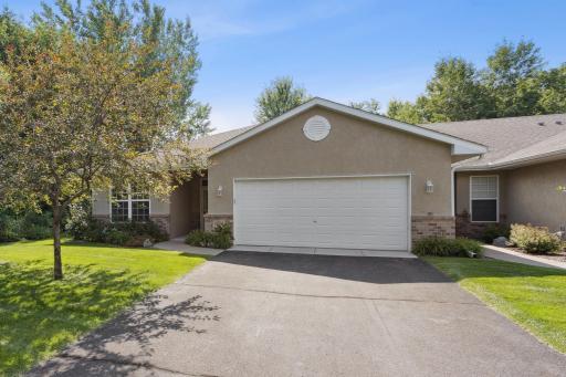 Charming front exterior with a classic stucco and brick finish, beautifully landscaped yard, mature tree, and a spacious two-stall garage. Quiet, well-kept neighborhood setting.