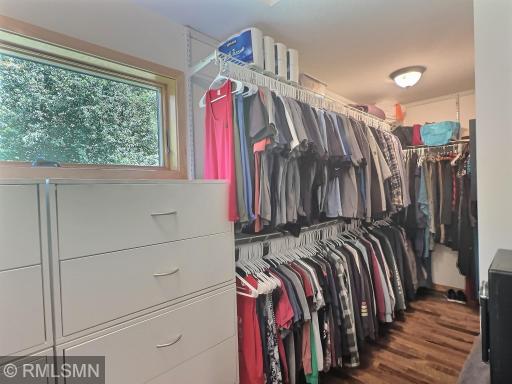 A large walk-in closet features hanging racks, shelves, drawers, and even a window for natural light.