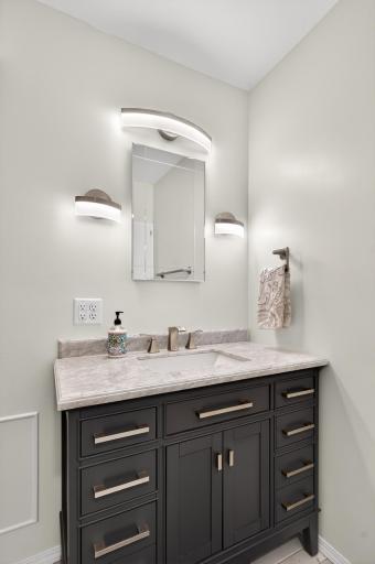 The sink vanity has a granite surface with an under-mounted sink basin, with brushed nickel cabinet drawer pulls matching the faucet, towel hook and towel bars.