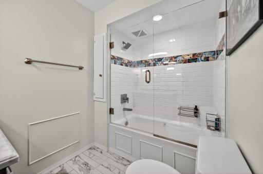 Remodeled in 2020, the lower level full bath features a jacuzzi-style bathtub with a ceramic tile surround with a beveled glass shower door.